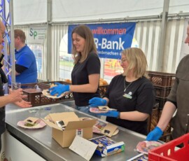 Volunteer in a black shirt with blue gloves hands a plate to a man at a food booth in a tent.