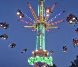Colorful illuminated swing ride at a fair, riders enjoying a circular flight against a twilight sky